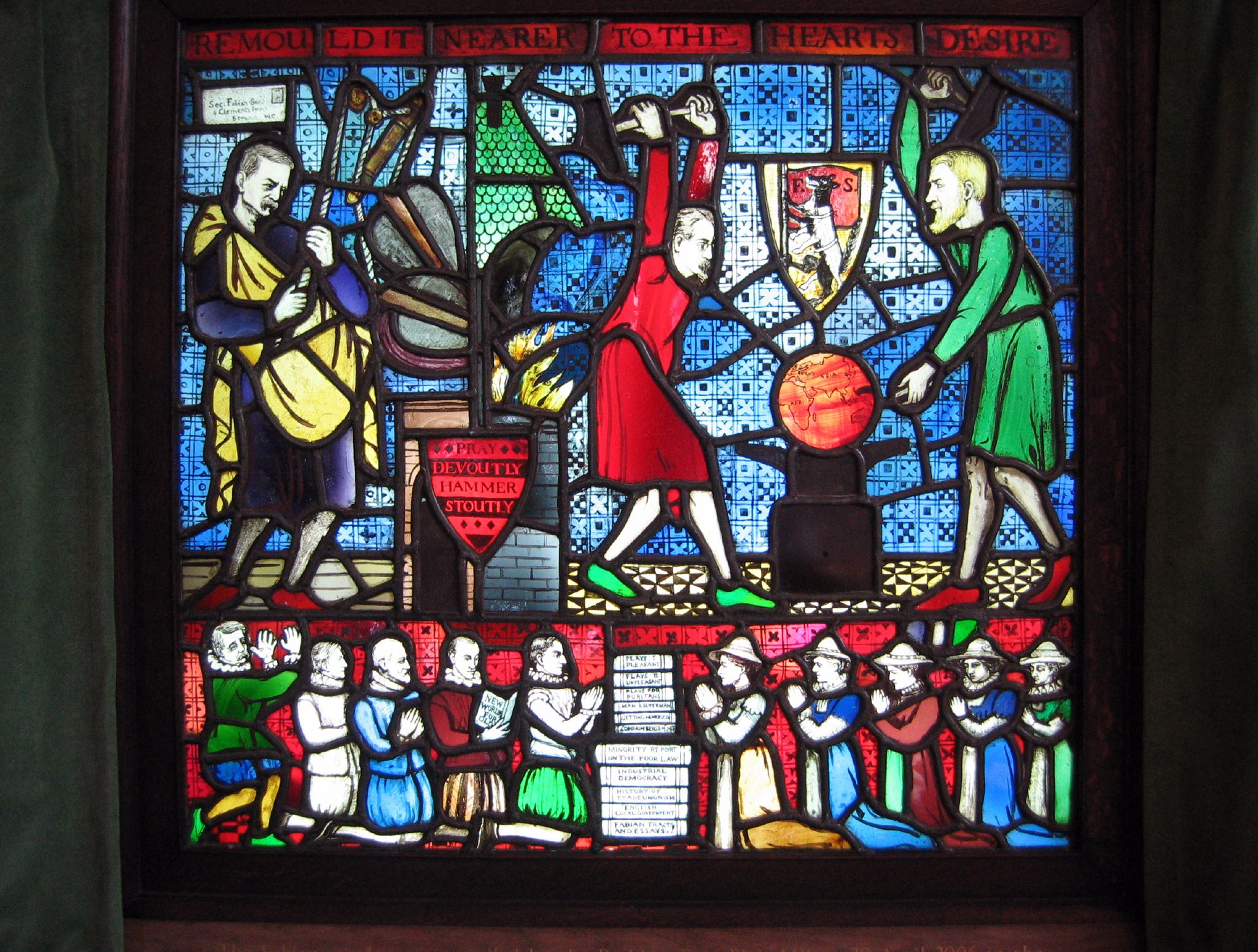 The Fabian Window: two robed figures, Shaw and Sidney Webb, hammering a globe on an anvil beneath a coat of arms showing a wolf in sheep's clothing, with the inscription REMOULD IT NEARER TO THE HEART'S DESIRE.